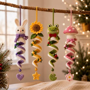 Könnte beinhalten: Vier gehäkelte Hängedekorationen bestehend aus einem weißen Hasen mit violettem Schal, einer gelben Sonnenblume, einem grünen Frosch mit roter Fliege und einem rosa Pilz. Jedes Ornament hat einen spiralförmigen Schwanz mit kleinen Perlen.