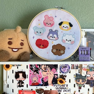 Könnte beinhalten: Ein runder Stickrahmen aus Holz mit weißem Stoff, der sieben farbenfrohe, im Kreuzstich gestickte Cartoon-Gesichter zeigt. Die Figuren umfassen rosa, gelbe, blaue, violette, rote, weiße und braune Designs mit kleinen Sternakzenten.