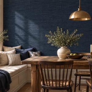 May include: A dining area featuring a dark navy blue textured wallpaper wall, a wooden table with spindle chairs, a beige cushioned bench with striped and solid pillows, a brass pendant light, and a ceramic vase with green branches.
