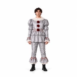 Puede incluir: Un disfraz de payaso gris plateado con cuello blanco de volantes, mangas abullonadas y cintura con volante. El conjunto incluye tres pompones de color rojo oscuro en la parte delantera, ribetes rojos a juego en la cintura y puños, y volantes.