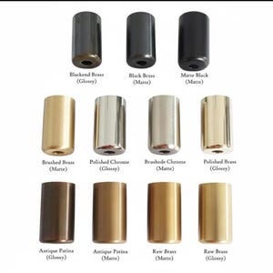May include: A collection of eleven cylindrical metal hardware components arranged in three rows. Finishes include Blackened Brass, Black Brass, Matte Black, Brushed Brass, Polished Chrome, Brushed Chrome, Polished Brass, and Antique Patina.