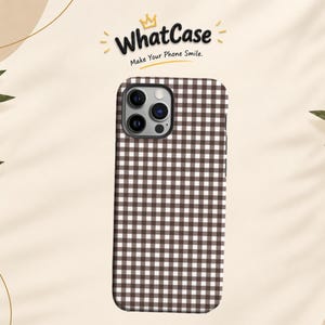 Puede incluir: Una funda para smartphone con un patrón de cuadros vichy en marrón y blanco. Sobre la funda, se muestra el texto WhatCase con un icono de corona y el eslogan Make Your Phone Smile. La funda tiene un recorte para un sistema de triple cámara.