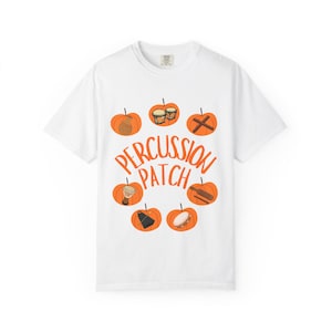 May include: A white short-sleeve t-shirt featuring a graphic of six orange pumpkins arranged in a circle. Each pumpkin contains a different percussion instrument illustration. The text PERCUSSION PATCH is printed in orange in the center.