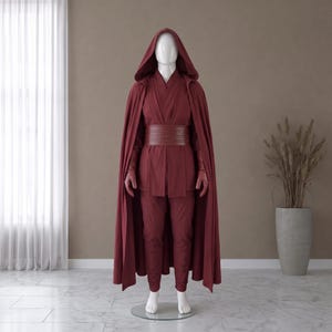 May include: A dark red costume set displayed on a mannequin, featuring a hooded cloak, a wrap-style tunic with long sleeves, matching trousers, a wide horizontal-panelled belt, and a pair of gloves, all in a uniform deep maroon colour palette.