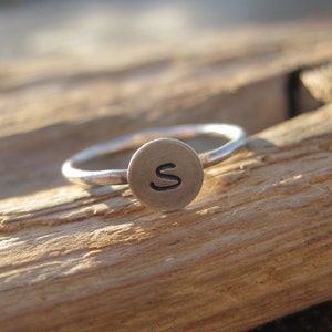 May include: A silver ring with a round, silver charm that has the letter "S" engraved on it.