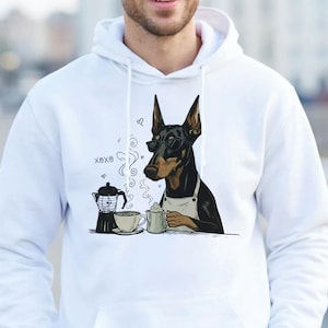 May include: A white hooded sweatshirt featuring a graphic illustration of a Doberman dog wearing glasses and an apron, sitting at a table with a coffee pot and a cup. The text X8X8 is printed near the coffee pot. The hoodie has long sleeves.