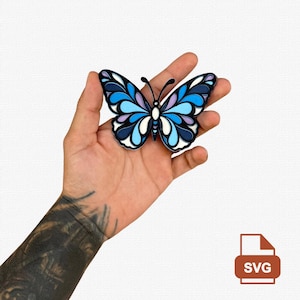 May include: A butterfly-shaped cutout featuring a layered design with shades of dark blue, light blue, white, and soft purple. The symmetrical wings display a series of rounded, petal-like segments outlined in black, with two thin antennae at the top.