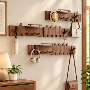 May include: Three wall-mounted wooden coat racks with integrated shelves and multiple hooks. The racks feature a slatted design and are holding a straw hat, a beige umbrella, white headphones, a beige handbag, and a brown leather shoulder bag.