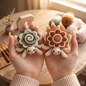 Puede incluir: Dos pequeñas tortugas de ganchillo con caparazones de motivos florales. Una tortuga tiene un caparazón en espiral verde y crema, y la otra un caparazón en forma de flor marrón y crema. Ambas tienen cuerpos color crema, ojos negros y mejillas rosas.