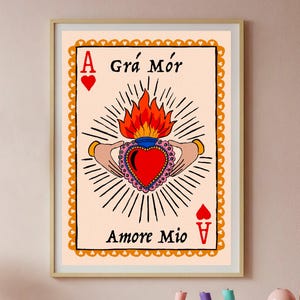 May include: A framed art print with an Ace of Hearts design. The artwork depicts a flaming heart held by hands, with the text "Grá Mór" and "Amore Mio". The card has a decorative border and a gold frame. The print is in a gold frame.