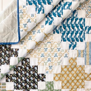 May include: A patchwork quilt with a variety of patterned squares. The quilt features squares with dog silhouettes, bows, floral designs, and other patterns in shades of blue, green, gold, and black. The quilt has a white backing with a blue border.