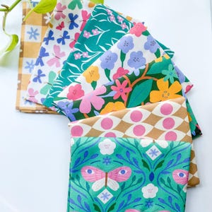 May include: A collection of folded fabric squares with various floral and butterfly patterns. The fabrics feature a range of colors, including pink, green, blue, and yellow. The designs include butterflies, flowers, and geometric shapes. The fabrics are arranged in a fan shape.