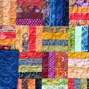 Puede incluir: Una colcha de patchwork que presenta una cuadrícula de tiras de tela rectangulares en varios colores, incluyendo rojo, azul, naranja, morado, verde y amarillo. Las piezas de tela muestran diversos patrones como lunares, flores y estampados.