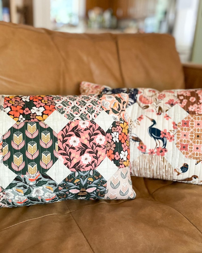 Two finished Honeycomb Pillows made with Honey Garden and Enchanted fabric collections by Cloud9 Fabrics, displayed on a brown leather couch. The quilted pillows feature a honeycomb-inspired patchwork design and are sewn in a 12" x 20" lumbar size.
