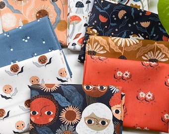 May include: A collection of folded fabric squares featuring various printed patterns including stylized suns with faces, mushrooms, flowers, and human figures with glasses. The color palette includes shades of orange, navy blue, white, and brown.