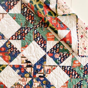 May include: A patchwork quilt featuring a mix of patterned fabrics in red, green, blue, and white. The quilt has repeating geometric shapes and a floral border. The quilt is made of soft fabric and has a quilted design.
