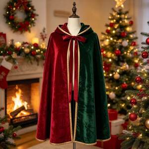 May include: A hooded cloak featuring a split design with one side in deep red velvet and the other in dark green velvet. The garment includes a gold braided trim along the edges and a matching red velvet ribbon tie closure at the neckline.