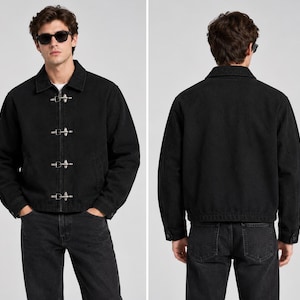 May include: A black denim jacket featuring a classic collar, long sleeves with buttoned cuffs, and a front closure secured by four silver-toned metal toggle clasps. The jacket has a straight hemline and a plain back, shown from both front and back views.