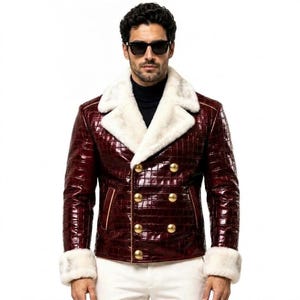 Puede incluir: Una chaqueta de doble botonadura en color burdeos intenso con una textura brillante de piel de cocodrilo en relieve. Presenta un cuello ancho de piel sint&eacute;tica blanca y pu&ntilde;os de piel sint&eacute;tica a juego, con seis botones dorados redondos.