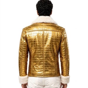 Puede incluir: Una chaqueta dorada metalizada con un patr&oacute;n texturizado de piel de cocodrilo, un cuello ancho de piel sint&eacute;tica blanca y pu&ntilde;os de piel sint&eacute;tica blanca a juego en las mangas largas. La chaqueta se lleva sobre pantalones blancos, vista de espaldas.