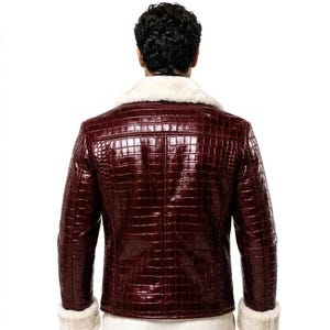 Puede incluir: Una chaqueta de color burdeos oscuro con una textura brillante que imita la piel de cocodrilo. La chaqueta presenta un cuello grueso de piel sint&eacute;tica blanca y pu&ntilde;os de piel sint&eacute;tica blanca a juego en los extremos de las mangas largas.
