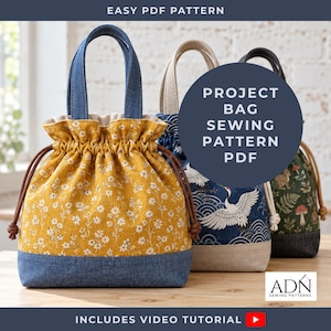 May include: Three drawstring project bags with fabric handles. The front bag is mustard yellow with a white floral print and a blue denim base. The middle bag is blue with a white crane and wave print. The back bag is dark green with a mushroom print.