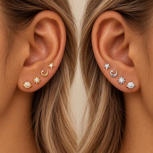 May include: A set of four celestial-themed stud earrings arranged in a row on an earlobe. The set includes a star, a crescent moon with a small stone, a sun with a central stone, and a planet with a ring and stone accents, available in gold and silver.