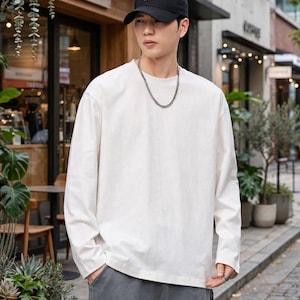 May include: A long-sleeve off-white crew neck shirt, a black baseball cap with a small white logo, a silver chain necklace, and dark gray cargo pants with visible pockets. The shirt features a plain, solid-colored fabric design.