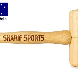 May include: A light-coloured wooden mallet with a cylindrical head and a contoured handle. The text SHARIF SPORTS is engraved in a dark, sans-serif font along the length of the handle. The wood grain is visible throughout the entire object.