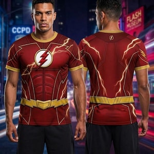 May include: A short-sleeved red t-shirt featuring a printed Flash superhero costume design. The front displays a circular yellow emblem with a red lightning bolt, while both sides show yellow lightning patterns, a gold collar, and a gold belt graphic.