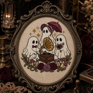May include: A cross-stitch embroidery in an oval ornate bronze frame featuring three white ghosts. One ghost holds a pink umbrella, another a bouquet of dark flowers, and the third operates a brown gramophone. Red mushrooms and roses surround them.