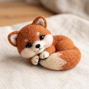 May include: A needle-felted fox figurine crafted from wool, featuring a vibrant orange coat with white accents on the face, ears, and tail tip. The fox has large black eyes, a small black nose, and is depicted in a curled, resting position.