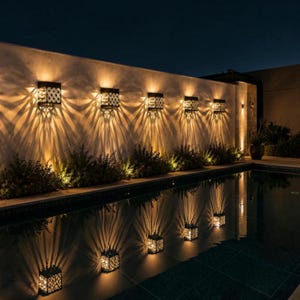 May include: Five square black wall-mounted outdoor light fixtures are arranged in a row on a light-colored wall. Each fixture emits a warm, bright light that creates a distinct, radiating starburst pattern on the wall above and below the unit.