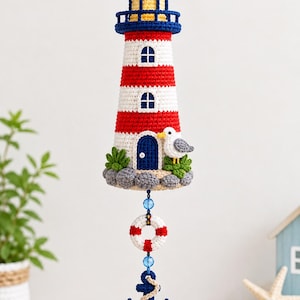 May include: A crocheted lighthouse hanging ornament featuring red and white horizontal stripes, a blue door, and a small seagull. Below the lighthouse hangs a white and red life preserver, a blue anchor with rope, and a blue tassel.