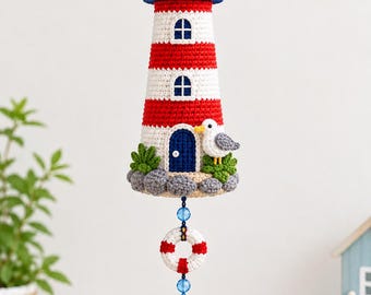 May include: A crocheted lighthouse hanging ornament featuring red and white horizontal stripes, a blue door, and a small seagull. Below the lighthouse hangs a white and red life preserver, a blue anchor with rope, and a blue tassel.