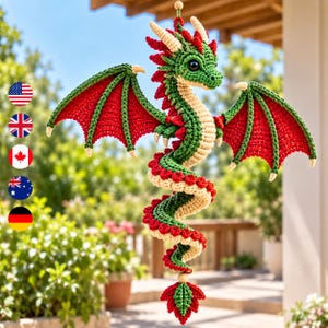 May include: A crocheted dragon ornament featuring a green body, a cream-colored underbelly, and vibrant red wings with green edges. The dragon has a coiled tail, small horns, and dark eyes, suspended by a string with a small wooden bead at the top.