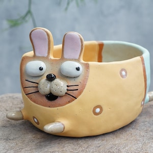 May include: A set of three ceramic mugs with a speckled, matte finish in cream, light grey, and dark grey. Each mug has a simple, minimalist design and a rounded handle.