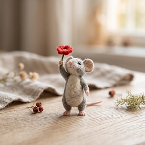 May include: A needle-felted mouse figurine with grey and cream-colored fur, standing upright and holding a small, vibrant red flower with a yellow center in one raised paw. The mouse has delicate whiskers, pink ears, and a small pink nose.