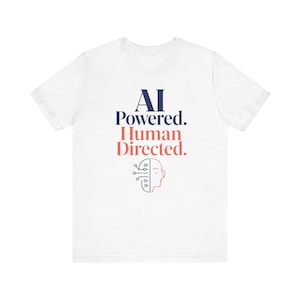 Puede incluir: Una camiseta blanca de manga corta con el texto azul oscuro AI POWERED. y el texto rojo coral Human Directed. Debajo del texto hay un gráfico de una cabeza humana dividida en un patrón de placa de circuito y un perfil humano.