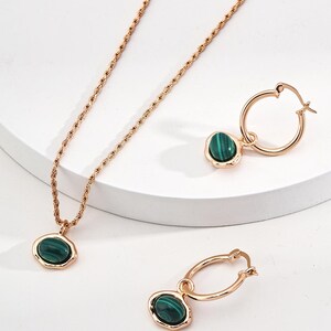May include: A jewelry set consisting of a rope chain necklace and two hoop earrings, all crafted in a rose gold tone. Each piece features a smooth, oval-shaped green malachite stone with dark banded patterns set in a simple metal bezel.