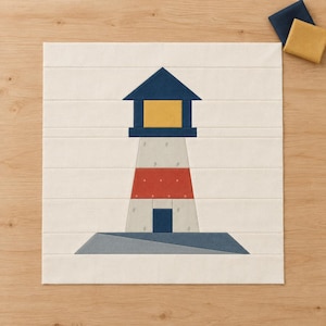 May include: A square fabric quilt block featuring a lighthouse design. The lighthouse has a dark blue roof, a yellow light section, a light gray tower with a red horizontal band, and a dark blue base set against a cream-colored background.