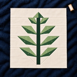 May include: A square fabric quilt block featuring a central dark green vertical stem with four pairs of symmetrical leaves extending outwards. The leaves are composed of light and dark green fabric segments with small white botanical patterns.