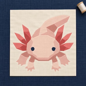 May include: A square fabric quilt block featuring a geometric, pieced axolotl design in shades of light pink and coral. The creature has dark blue eyes, prominent feathery gills, and a curved tail, all constructed from angular fabric shapes.