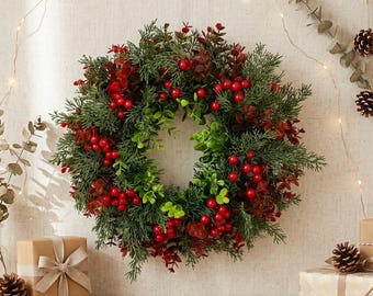 May include: A circular wreath featuring dense green pine-like foliage, vibrant red berries, and small dark red leaves. The arrangement is constructed with a mix of textures, creating a full, rounded appearance with a hollow center for display.