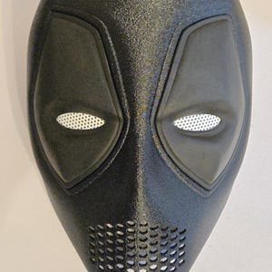 Può includere: Una maschera integrale nera con finitura testurizzata, dotata di due aperture per gli occhi a forma di mandorla coperte da una rete bianca, una sezione frontale perforata e un'area della bocca perforata, dal design sagomato e slanciato.