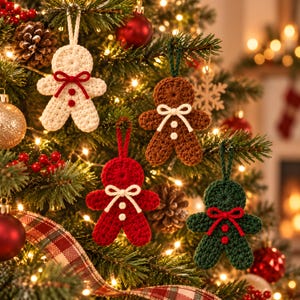 Könnte beinhalten: Vier gehäkelte Lebkuchenmann-Anhänger hängen an einem Weihnachtsbaum. Das Set enthält eine cremefarbene, eine braune, eine rote und eine dunkelgrüne Figur, die jeweils mit einer kontrastierenden Schleife und zwei kleinen Knöpfen versehen sind.