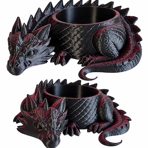 Peut inclure: Deux pots de fleurs en forme de dragon noir et rouge foncé. Chaque pièce représente un dragon enroulé avec des écailles détaillées, une rangée de pointes sur le dos et une ouverture circulaire au centre. La finition est noir mat avec des reflets rouges.