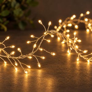 May include: A string of decorative fairy lights featuring thin, flexible silver-toned wire branches. Each branch terminates in a small, warm white LED bulb shaped like a tiny teardrop, creating a cluster of glowing points of light.