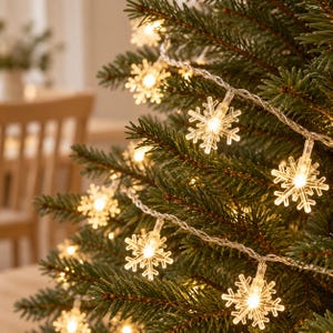 以下が含まれることがあります： 透明なプラスチック製の雪の結晶の形をしたLEDライトのストリングが、クリスマスツリーの緑の針葉に飾られています。それぞれの雪の結晶のオーナメントには、暖かみのある白色の小さなLED電球が入っており、明るく輝いてお祝いの雰囲気を演出しています。
