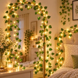 Peut inclure: Une guirlande de lierre artificiel composée de feuilles vertes en forme de cœur entrelacées de guirlandes lumineuses LED blanc chaud. La guirlande est drapée sur un miroir sur pied arqué et le long du haut d'une tête de lit capitonnée.